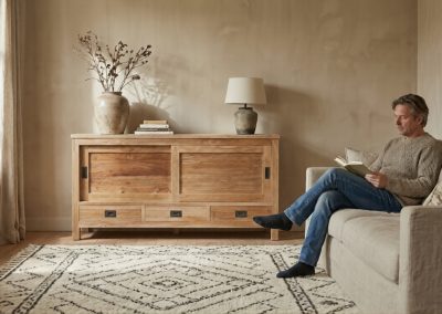 Man leest op bank naast teak dressoir Bumi Low 150 cm met vaas en vloerkleed