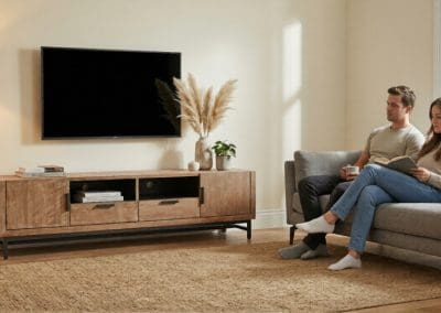 Koppel kijkt tv op grijze bank met teak tv dressoir Selaras en vloerkleed in woonkamer